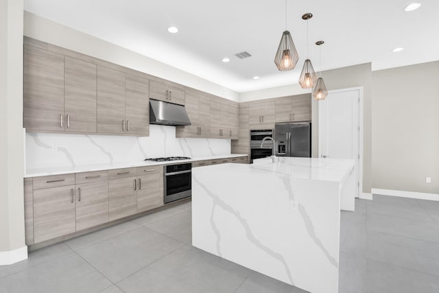 kitchen featuring stainless steel appliances, under cabinet range hood, an island with sink, light stone countertops, and hanging light fixtures