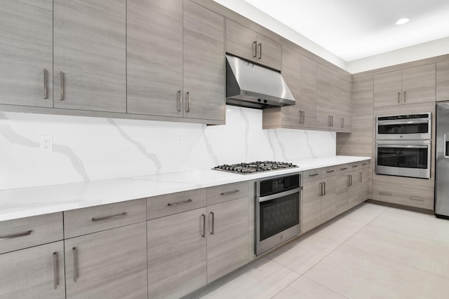 kitchen with gray cabinetry, under cabinet range hood, light tile patterned floors, modern cabinets, and appliances with stainless steel finishes