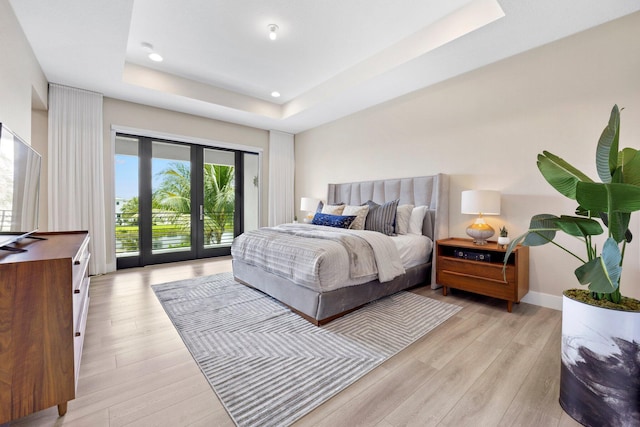 bedroom featuring light wood finished floors, access to exterior, baseboards, a raised ceiling, and recessed lighting