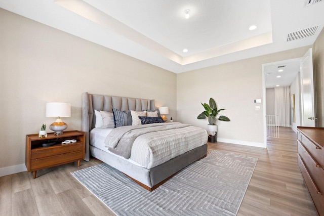bedroom featuring recessed lighting, baseboards, light wood finished floors, visible vents, and a raised ceiling