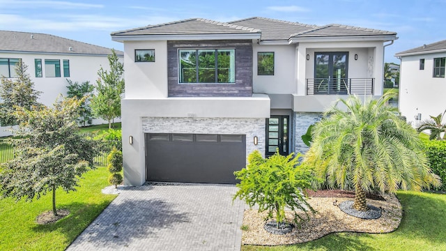 modern home with stucco siding, decorative driveway, a garage, and a balcony