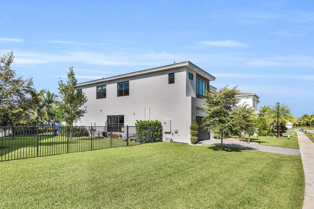 rear view of property featuring an attached garage, stucco siding, fence, a lawn, and driveway