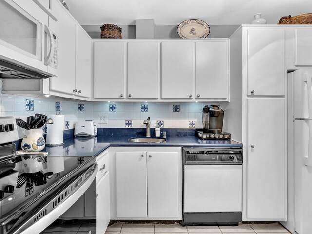 kitchen featuring light tile patterned floors, white cabinets, a sink, dark countertops, and white appliances