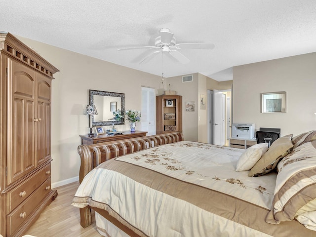 bedroom with light wood-style floors, a textured ceiling, a ceiling fan, visible vents, and baseboards