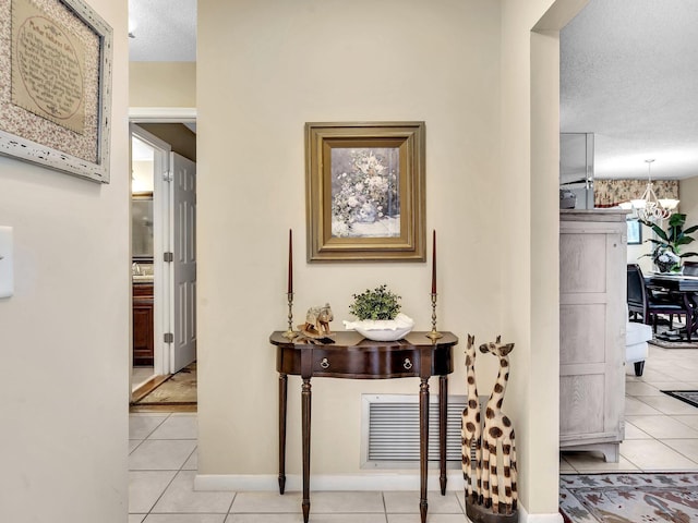 corridor featuring light tile patterned floors, visible vents, a textured ceiling, and an inviting chandelier