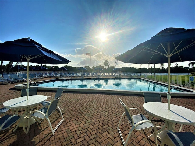 community pool with a patio area, fence, and outdoor dining area