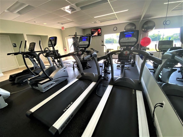 exercise room featuring a paneled ceiling, visible vents, and a healthy amount of sunlight