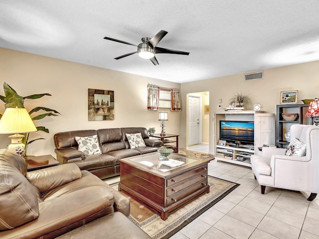 living room featuring light tile patterned floors, visible vents, a textured ceiling, and ceiling fan