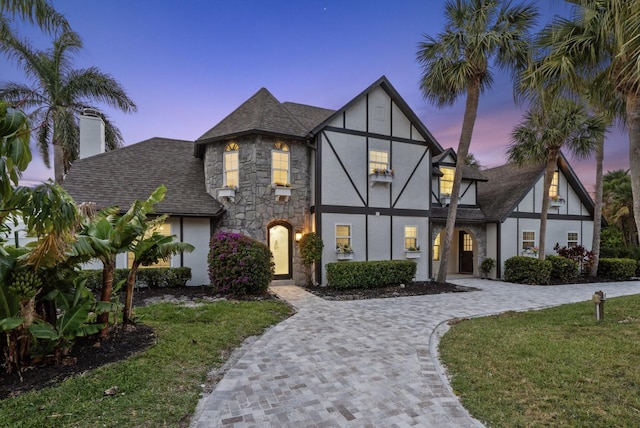 121 Queen Eugenia Ct, Hutchinson Island, FL 34949 - tudor home featuring stone siding, a lawn, stucco siding, driveway, and roof with shingles