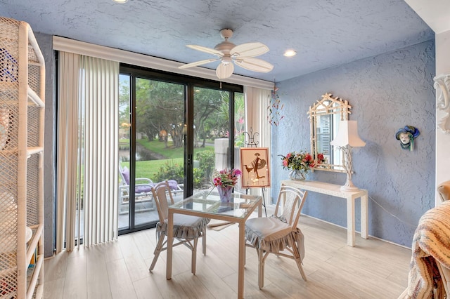 dining space with light wood-style floors, a textured wall, and a ceiling fan