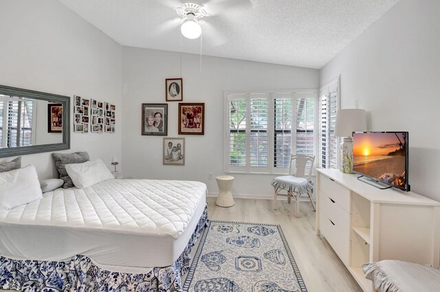 bedroom with light wood finished floors, a textured ceiling, vaulted ceiling, and a ceiling fan