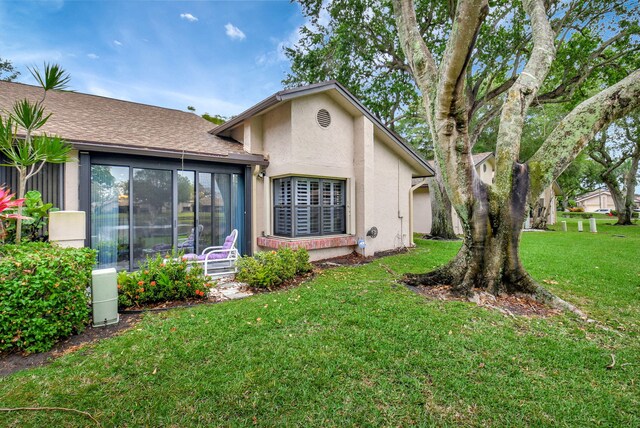 back of property with a yard, a sunroom, and stucco siding