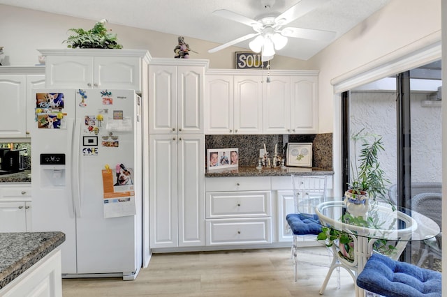 kitchen with light wood-style floors, white refrigerator with ice dispenser, white cabinets, dark stone countertops, and lofted ceiling