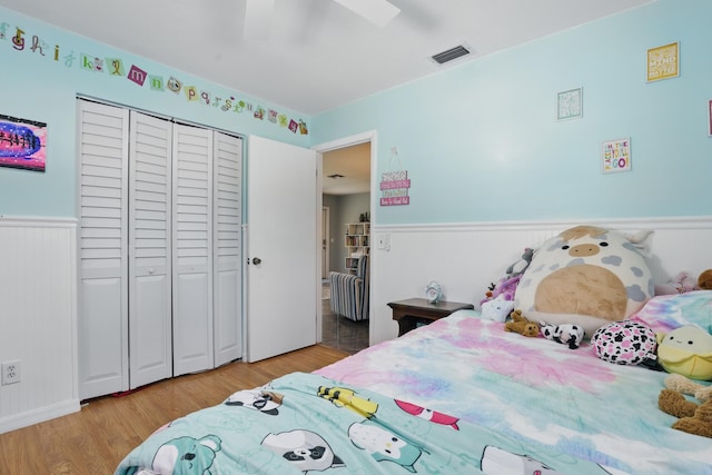 bedroom featuring a closet, a ceiling fan, visible vents, a wainscoted wall, and light wood finished floors