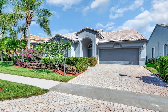 mediterranean / spanish-style house with an attached garage, a tiled roof, stucco siding, and decorative driveway
