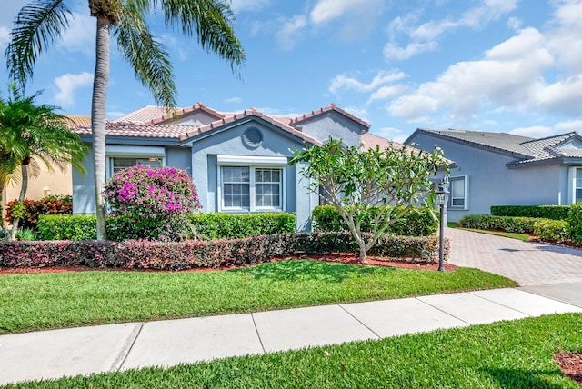 mediterranean / spanish home with a tiled roof, a front lawn, decorative driveway, and stucco siding