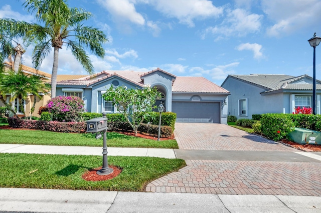 mediterranean / spanish-style house featuring stucco siding, decorative driveway, a tile roof, a front lawn, and an attached garage