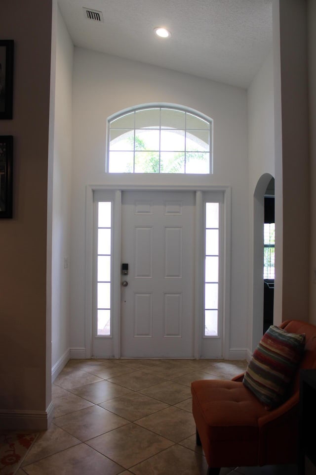 entrance foyer featuring arched walkways, a towering ceiling, baseboards, and visible vents