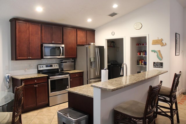 kitchen featuring light tile patterned floors, visible vents, a breakfast bar, vaulted ceiling, and stainless steel appliances