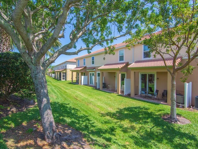 rear view of property with a tile roof, a yard, and stucco siding