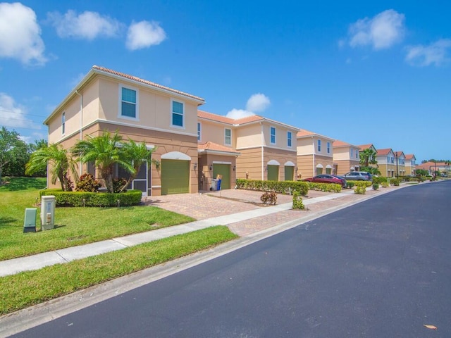 mediterranean / spanish-style home with an attached garage, driveway, stucco siding, a front lawn, and a residential view
