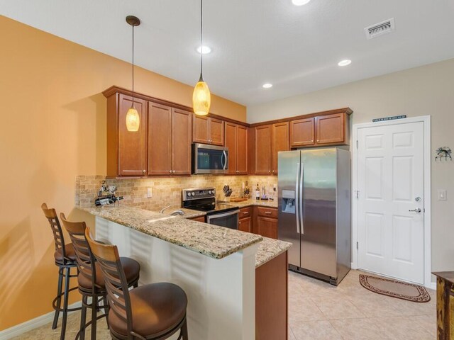 kitchen featuring stainless steel appliances, brown cabinets, a peninsula, tasteful backsplash, and light stone counters