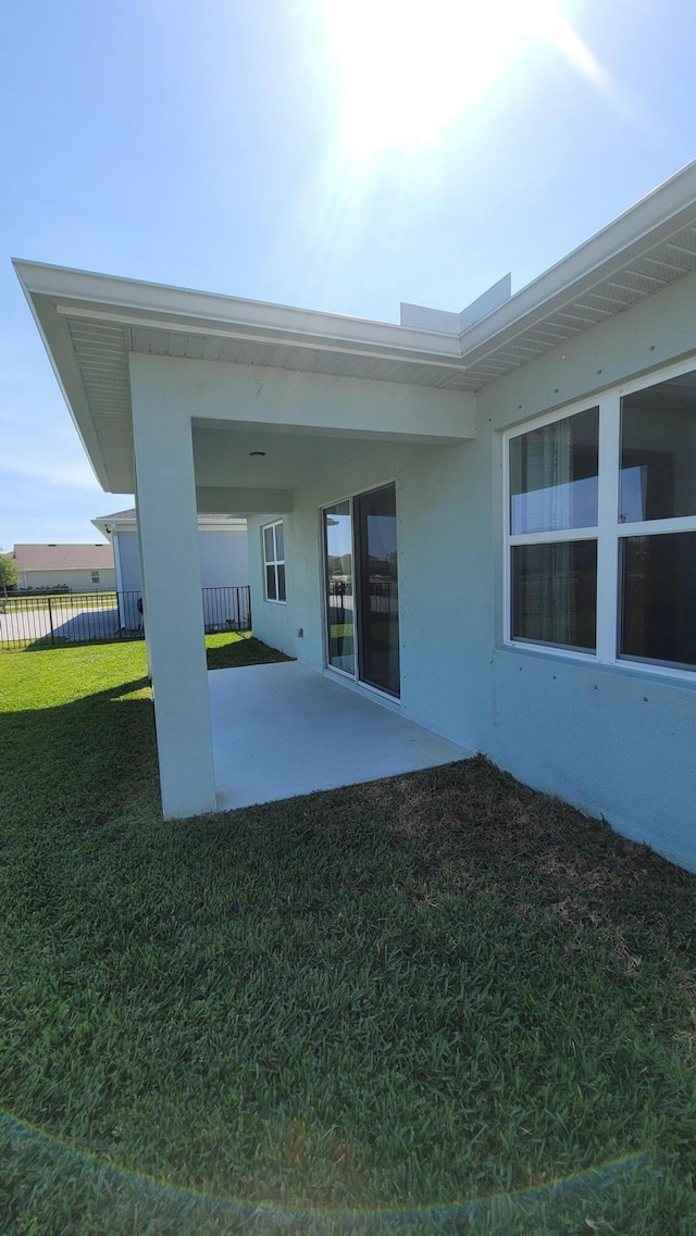 rear view of property featuring fence, stucco siding, a yard, and a patio area