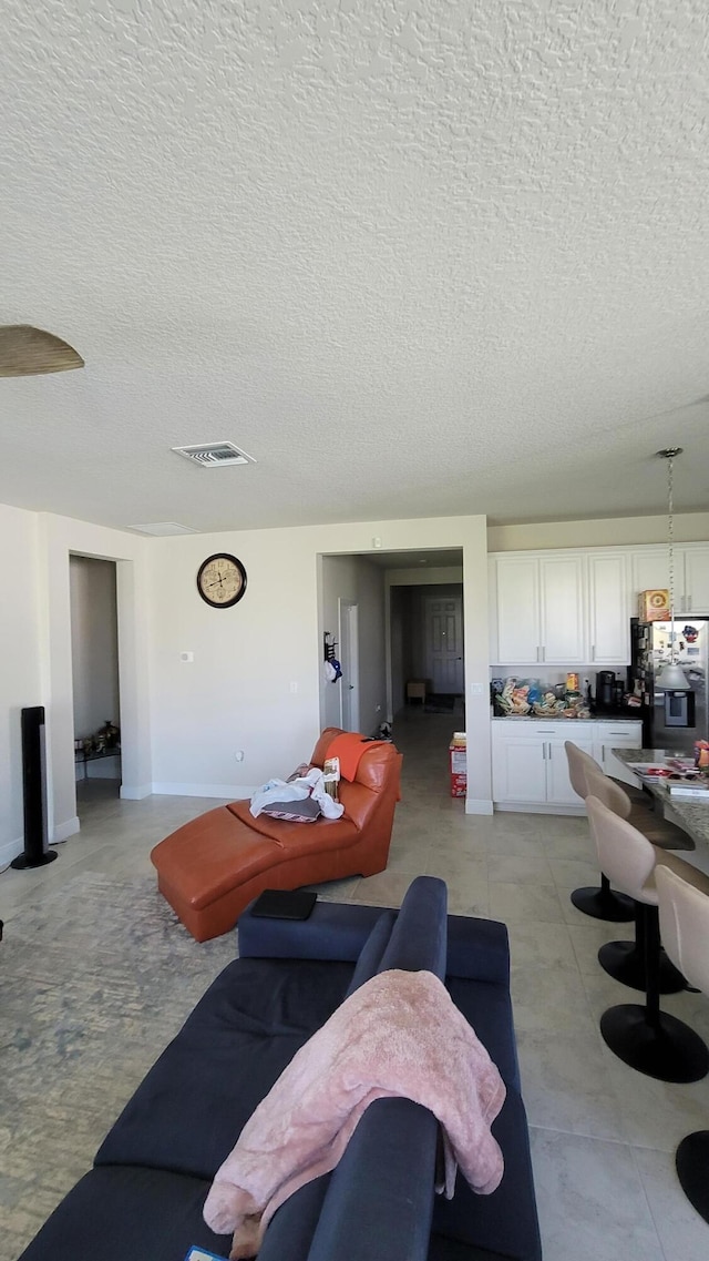 living area with a textured ceiling, visible vents, and baseboards