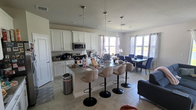kitchen with a breakfast bar area, visible vents, white cabinets, appliances with stainless steel finishes, and open floor plan