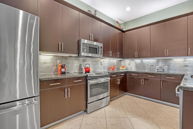 9068 Clearhill Rd, Boynton Beach, FL 33473 - kitchen with light tile patterned floors, dark brown cabinets, dark stone counters, decorative backsplash, and stainless steel appliances