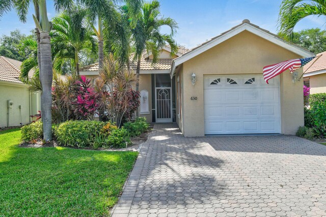 630 SW Treasure Cv, Port Saint Lucie, FL 34953 - view of front of home with a front lawn, decorative driveway, stucco siding, a tiled roof, and an attached garage