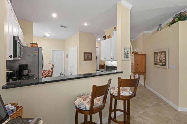 630 SW Treasure Cv, Port Saint Lucie, FL 34953 - kitchen with dark stone counters, a peninsula, stainless steel microwave, white cabinetry, and baseboards