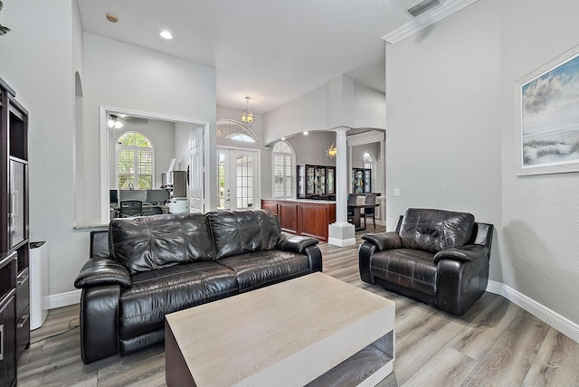 living room with decorative columns, arched walkways, french doors, and light wood-style flooring