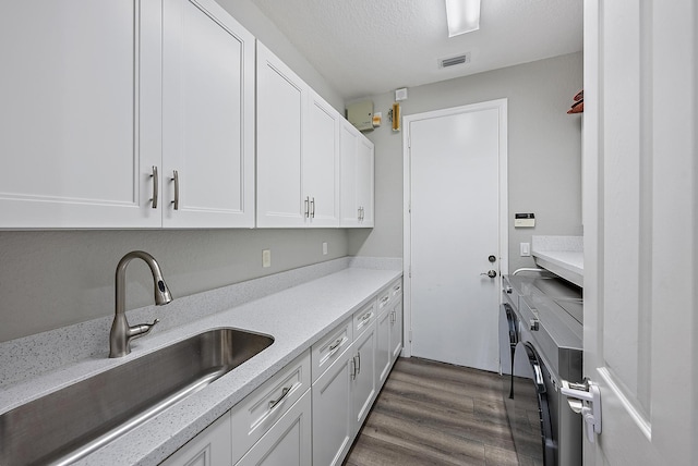 kitchen featuring dark wood-style flooring, a sink, white cabinetry, visible vents, and washing machine and clothes dryer