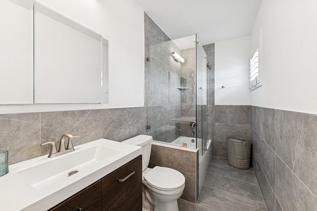 bathroom featuring toilet, tile walls, shower / bath combination with glass door, and vanity