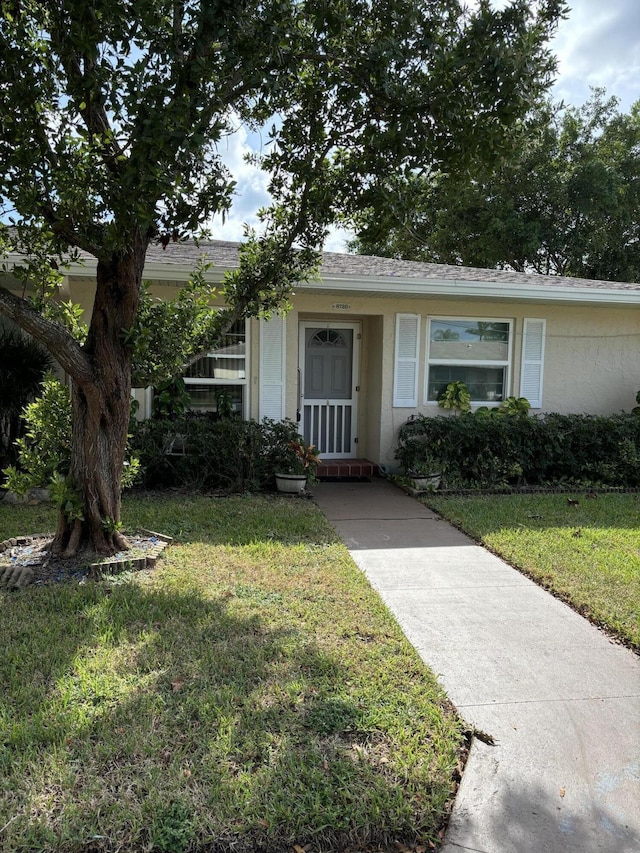 view of front facade featuring a front yard, stucco siding, and a shingled roof