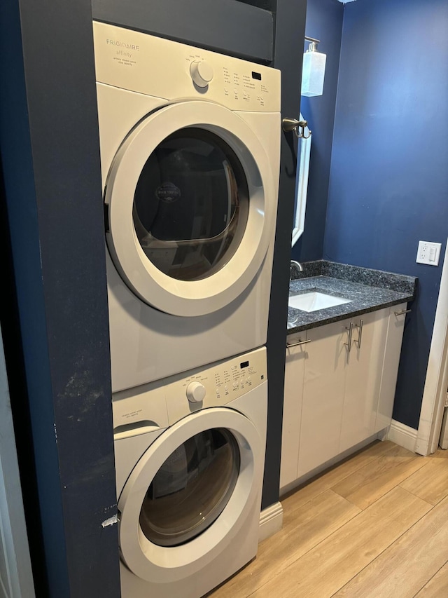 washroom featuring light wood-type flooring, a sink, stacked washer and clothes dryer, baseboards, and cabinet space