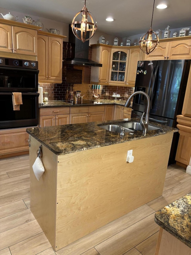 kitchen with wall chimney range hood, black appliances, a chandelier, a kitchen island with sink, and a sink