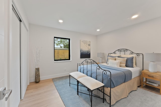 bedroom with a closet, recessed lighting, light wood-type flooring, and baseboards