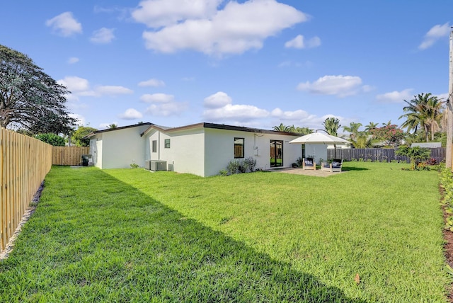 rear view of house with a fenced backyard, stucco siding, cooling unit, and a yard
