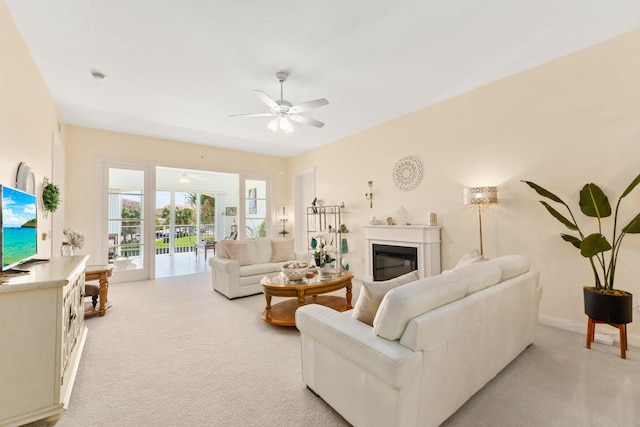 living room with ceiling fan, baseboards, a glass covered fireplace, and light colored carpet