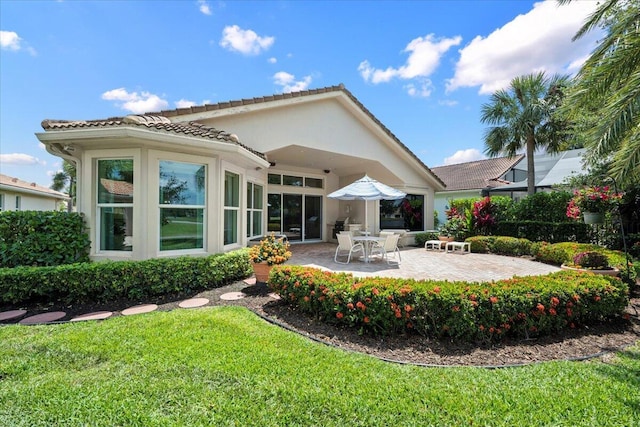 rear view of property featuring a patio area, a lawn, a tile roof, and stucco siding