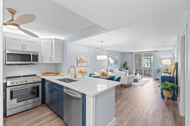 kitchen with appliances with stainless steel finishes, a sink, a peninsula, blue cabinetry, and light wood-style flooring