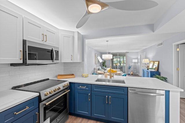 kitchen with appliances with stainless steel finishes, a peninsula, blue cabinetry, a sink, and white cabinets