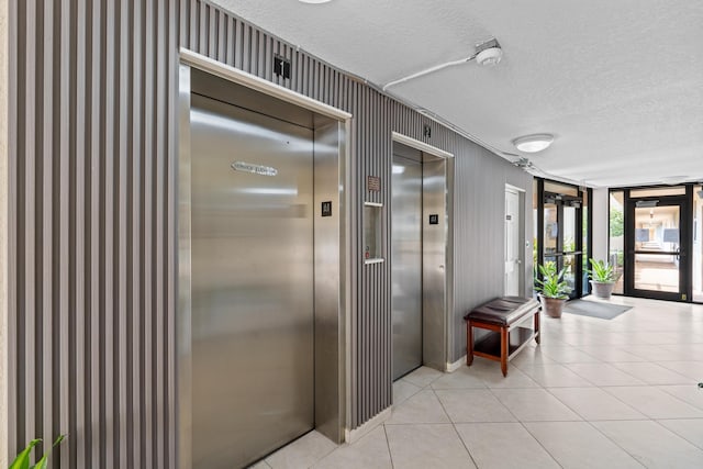 hall with elevator, a textured ceiling, and light tile patterned floors