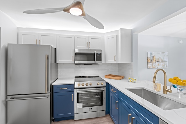 kitchen with appliances with stainless steel finishes, a sink, blue cabinets, tasteful backsplash, and light stone counters