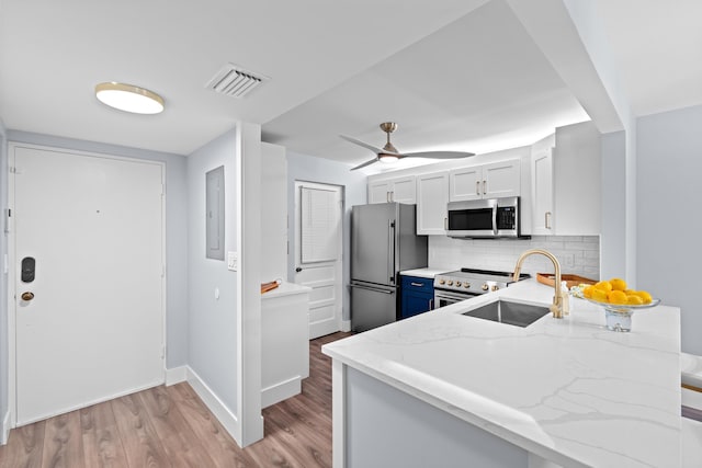 kitchen featuring stainless steel appliances, a sink, light stone countertops, light wood-style floors, and backsplash