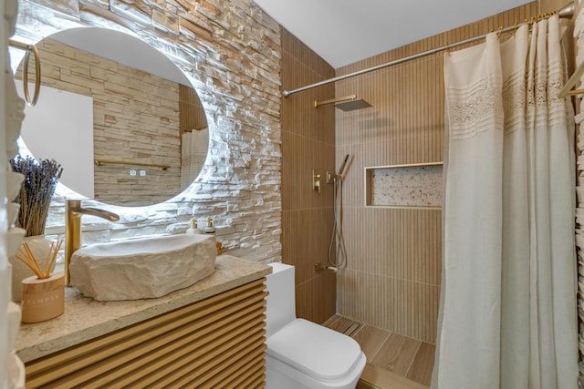 bathroom with tile walls, vanity, toilet, and tiled shower