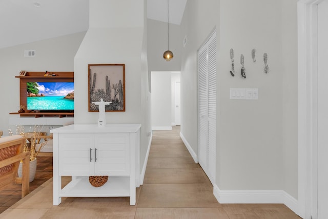 corridor featuring baseboards, light wood-style flooring, visible vents, and high vaulted ceiling