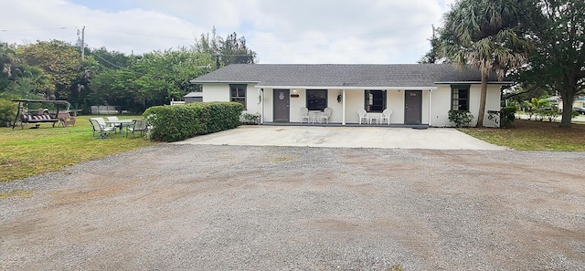 ranch-style home featuring stucco siding, driveway, a front yard, a porch, and a shingled roof